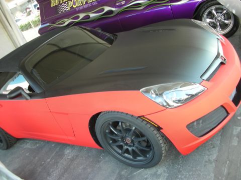 1998 Ford Crown Victoria - two-tone matte black and red sports car on black wheels sits beside a purple flamed muscle car under a canopy.