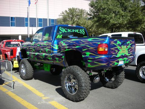 1998 Ford Crown Victoria - Rear three-quarter of a lifted custom truck with green-purple flames and a SICKNESS windshield banner.