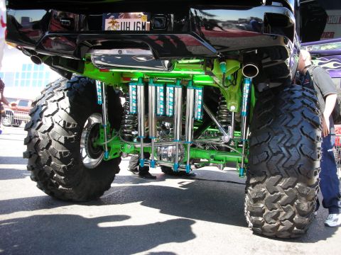 1998 Ford Crown Victoria - View under a lifted truck showing green-painted suspension, coilover shocks, and large off-road tires.