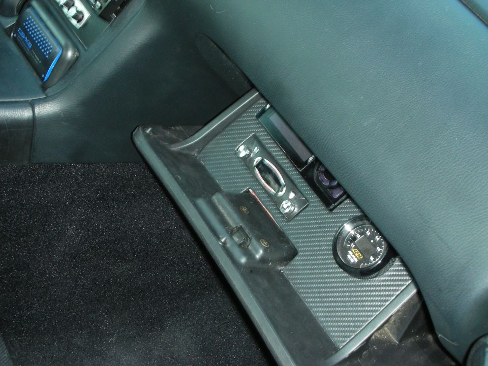 Car interior trim panel with carbon-fiber finish and a small round gauge