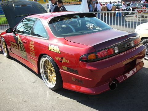 1998 Ford Crown Victoria - Rear three-quarter of a red wide-body Nissan coupe on gold wheels covered in sponsor decals.