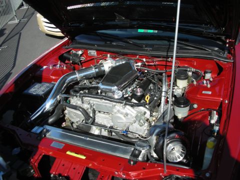 1998 Ford Crown Victoria - engine bay of a red sport coupe showing a polished cold-air intake and aluminum strut tower bar.