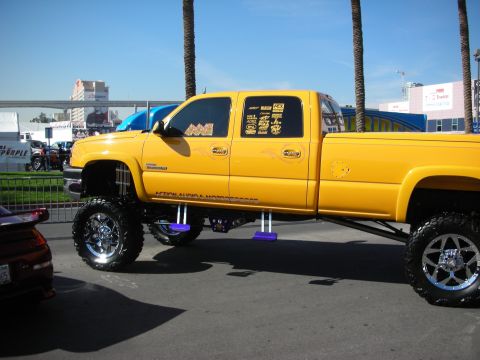 1998 Ford Crown Victoria - yellow lifted crew-cab diesel pickup on chrome wheels displayed outdoors at a show.