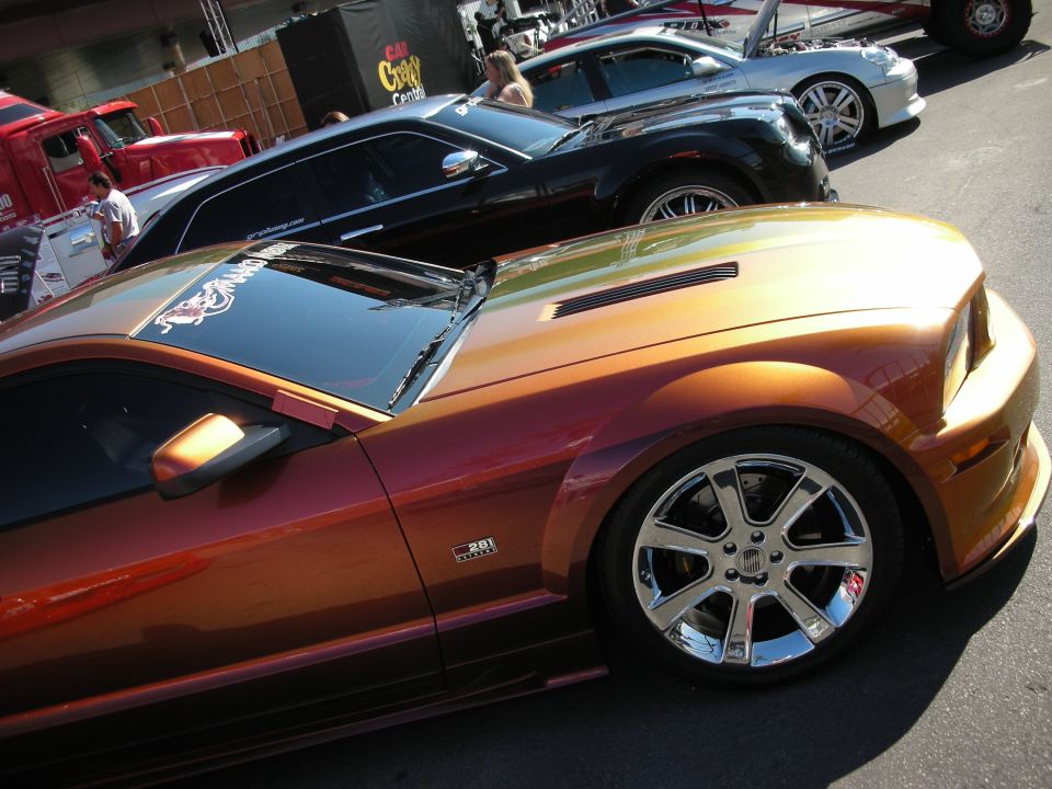 Copper-orange Ford Mustang with chrome wheels among show cars outdoors