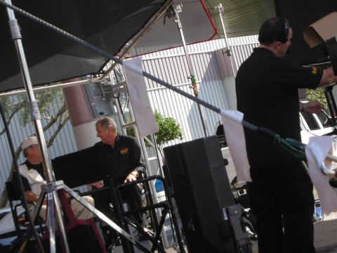 1998 Ford Crown Victoria - camera operator films two seated men during an outdoor interview shoot under a canopy.