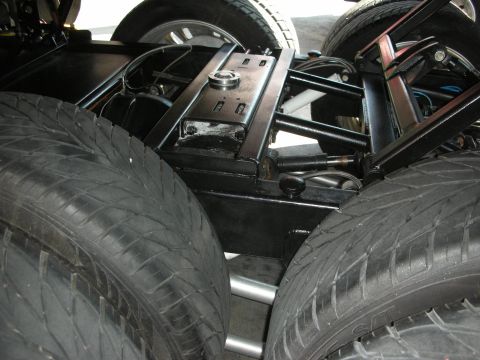 1998 Ford Crown Victoria - Close underside view of a vehicle's black-painted chassis and suspension between two pairs of wide rear tires.