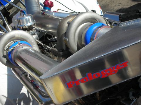 1998 Ford Crown Victoria - Close-up of a polished turbocharger, intake piping with blue couplers, and a stainless plenum lettered Prologger in red.