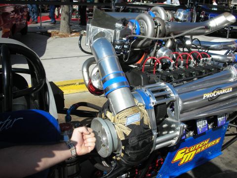 1998 Ford Crown Victoria - person's hand reaches toward a chrome ProCharger supercharged dragster engine on a blue rail car at an outdoor show.