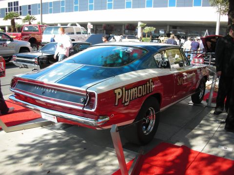 1998 Ford Crown Victoria - Rear three-quarter view of a red Plymouth Barracuda fastback with gold Plymouth lettering on a red display ramp.