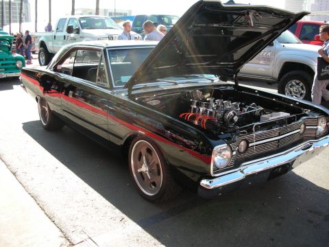 1998 Ford Crown Victoria - black Dodge Dart with a red side stripe, open hood revealing a chrome fuel-injected engine, parked among other show cars.
