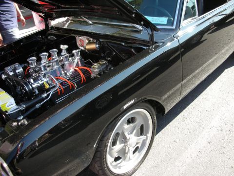 1998 Ford Crown Victoria - black classic car with raised hood revealing a chrome dual-quad carbureted V8 with orange plug wires and a polished wheel.