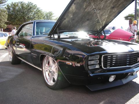 1998 Ford Crown Victoria - black first-generation Chevrolet Camaro Z/28 sits with its hood up and white-striped accents at a sunny car show.