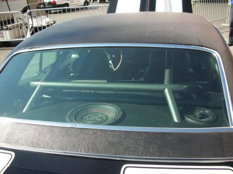 1998 Ford Crown Victoria - Through a black convertible's rear glass a chrome roll bar and rear bench seat are visible at a car show.