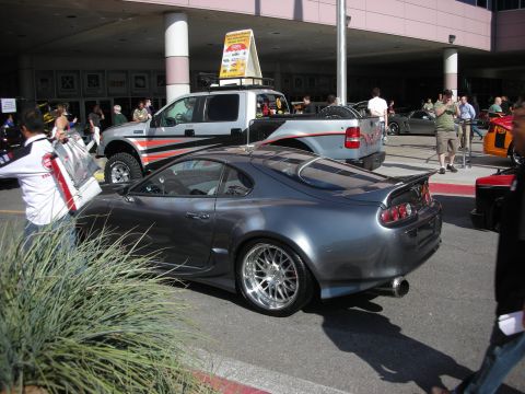 1998 Ford Crown Victoria - grey two-door sports coupe with a tall rear wing and chrome wheels is parked beside a lifted pickup at a show.