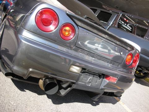 1998 Ford Crown Victoria - low-angle rear shot of a grey Nissan Skyline reveals its SKYLINE badge, round taillights and twin exhaust tips.