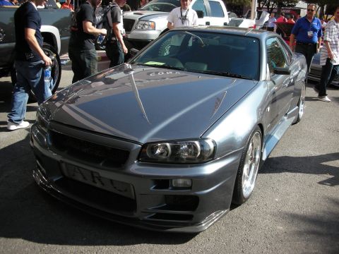 1998 Ford Crown Victoria - grey Nissan Skyline coupe with an aero front bumper and multi-spoke wheels is parked among crowds at a show.