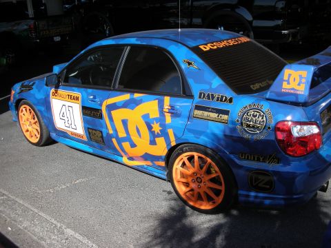 1998 Ford Crown Victoria - blue-camouflage Subaru Impreza rally sedan wears DC Shoes livery, number 41 and bright orange wheels.
