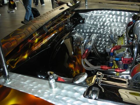 1998 Ford Crown Victoria - polished sheet-metal compartment holds braided fuel lines with red and blue AN fittings beneath a flame-painted lid.