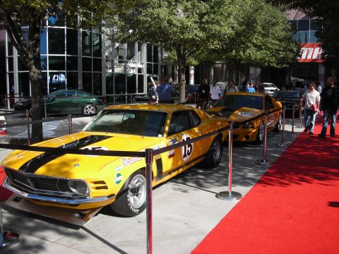 1998 Ford Crown Victoria - yellow-and-black classic Ford Mustang fastback wearing number 15 is displayed on a red carpet at a show.
