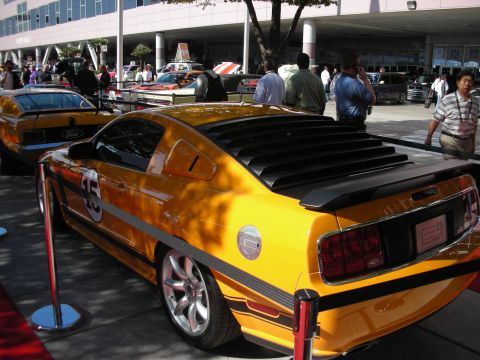 1998 Ford Crown Victoria - modern yellow-and-black Ford Mustang with rear window louvers and number 15 sits among display cars at an event.