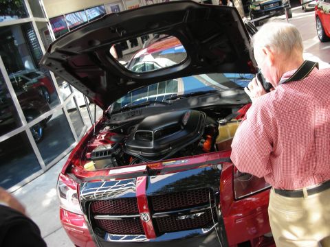 1998 Ford Crown Victoria - older man photographs the engine of a dark red Dodge displaying a black shaker-style hood scoop.