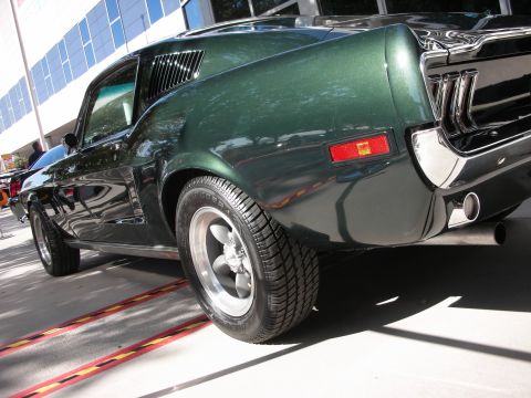 1998 Ford Crown Victoria - dark green classic fastback muscle car shown in rear three-quarter view with chrome exhaust and five-spoke wheels.