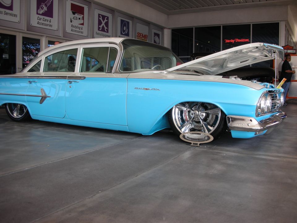 Light blue lowered classic sedan with hood up in a shop showroom