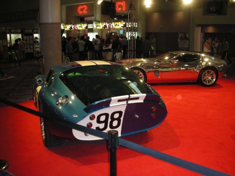 1998 Ford Crown Victoria - blue and white number 98 coupe race car sits beside a polished chrome concept car on red carpet at an indoor show.