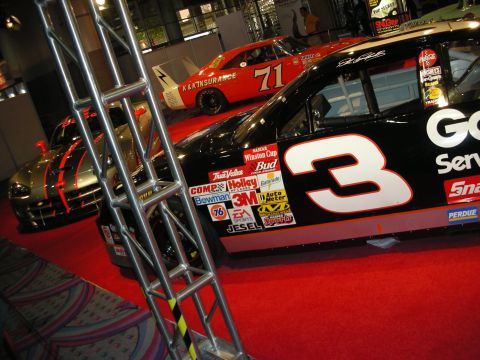 1998 Ford Crown Victoria - black number 3 Goodwrench stock car covered in sponsor decals sits beside an orange number 71 racer on red carpet.