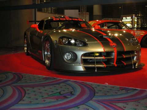 1998 Ford Crown Victoria - gunmetal Dodge Viper race car with red stripes, a front splitter and wide aero kit sits on patterned show carpet.