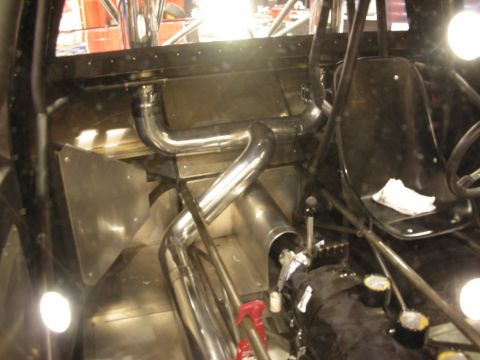 1998 Ford Crown Victoria - Bare tube-chassis race car interior showing the roll cage, stainless exhaust routing, shifter and single black bucket seat.