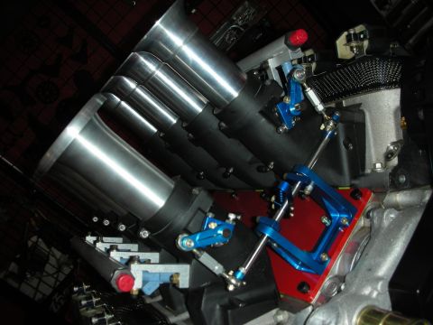 1998 Ford Crown Victoria - Angled close-up of a row of polished cylindrical individual throttle bodies with blue linkage brackets on a red manifold.
