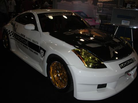 1998 Ford Crown Victoria - White Nissan 350Z coupe with black graphics, gold-tinted headlights and gold wheels wearing Koyorad and Falken sponsor decals.