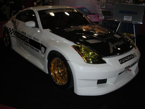 1998 Ford Crown Victoria - Front-three-quarter view of the same white Nissan 350Z coupe with gold wheels and Koyorad and Falken sponsor graphics.