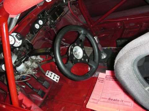 1998 Ford Crown Victoria - Bare red race-car interior with welded roll cage, mounted gauges, a small suede steering wheel and a Seals-it info card.