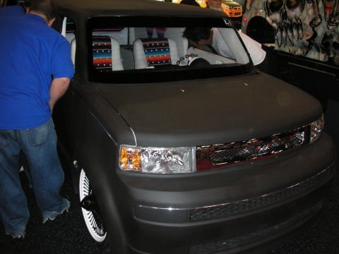1998 Ford Crown Victoria - Lowered matte-gray Scion xB box-shaped car with chrome wheels and a colorful Serape-pattern custom interior on display.