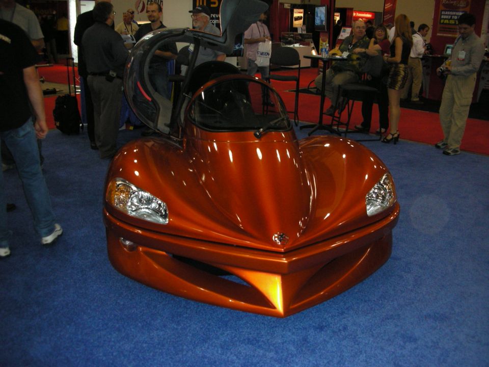 Orange teardrop-shaped concept car with bubble canopy at an expo