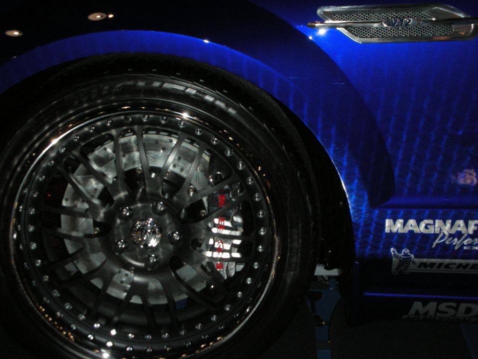 Black multi-spoke wheel with red brake caliper on a blue car