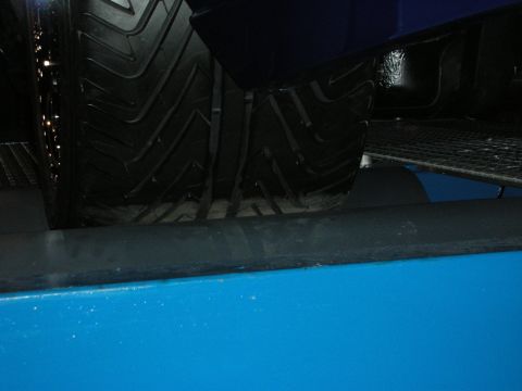 1998 Ford Crown Victoria - Dim close-up of a treaded tire and lower body of a blue vehicle parked over metal grating.