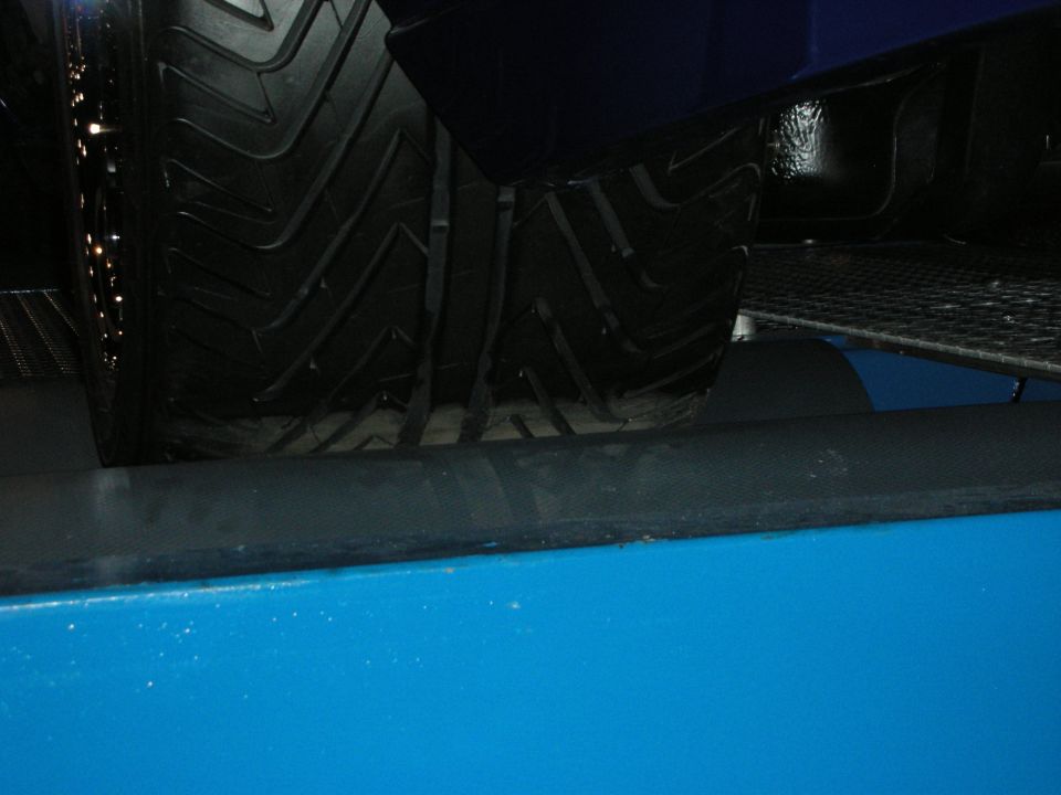 Close-up of a tire on a blue vehicle over grating, dim lighting