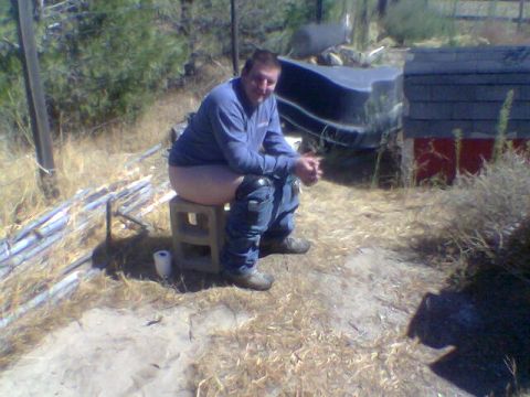 1988 Ford Bronco - A man is seated on a cinder block, appearing to use it as a makeshift toilet in an outdoor, dry environment.