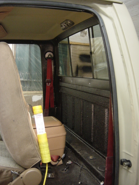 1991 Ford Bronco - The interior of an older model truck, possibly from the 1980s, shows a tan seat, red seatbelt, and storage bin.