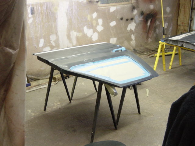 Car door with window opening taped off, resting on sawhorses in a workshop