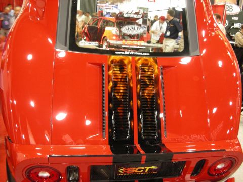 1998 Ford Crown Victoria - Rear of a red mid-engine sports car showing flame-painted engine covers under a glass hatch at a trade show.