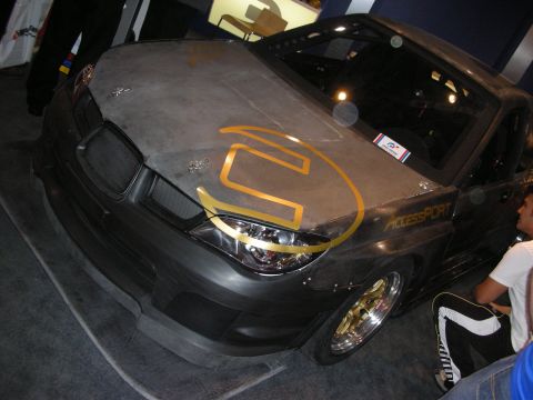 1998 Ford Crown Victoria - Front of a sports car wrapped in bare carbon-fiber bodywork with a gold logo and AccessPort decal on the fender.