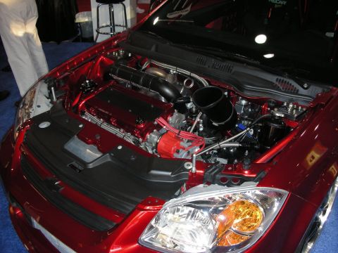1998 Ford Crown Victoria - Engine bay of a dark red Chevrolet compact car showing a red intake plenum, coil cover and amber headlight.