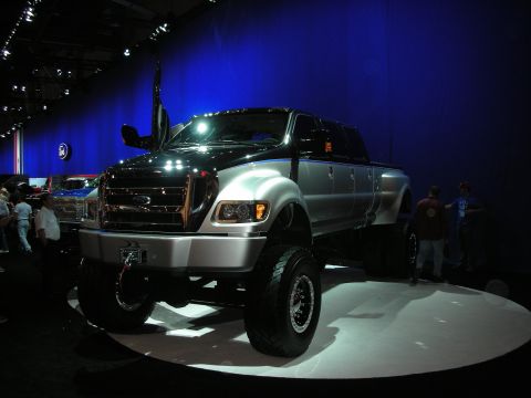1998 Ford Crown Victoria - massive lifted silver Ford F-650 crew cab truck displayed on a turntable under blue stage lighting.