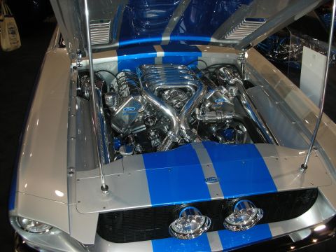 1998 Ford Crown Victoria - polished chrome engine sits in a silver-and-blue-striped Mustang with the hood raised, Ford script visible.
