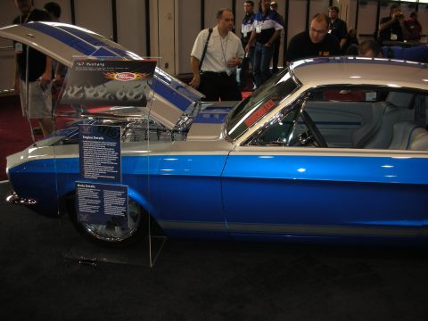 1998 Ford Crown Victoria - Side view of a blue and white custom Mustang fastback with raised hood and a '67 Mustang display placard at a show.
