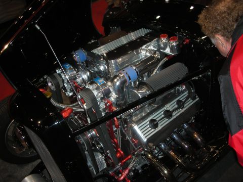 1998 Ford Crown Victoria - heavily chromed V8 engine topped with twin centrifugal superchargers and red fittings fills the bay of a black hot rod.